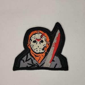 May include: Embroidered patch featuring a character wearing a hockey mask and holding a bloody knife. The character is wearing a grey jacket and an orange bandana. The patch is black with white and red stitching.