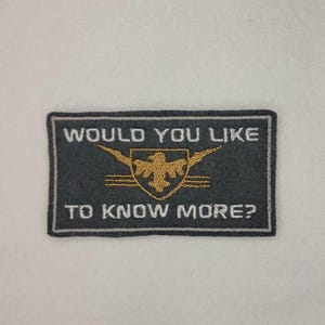 Puede incluir: Un parche bordado negro y gris con un diseño de águila blanca y el texto "Would you like to know more?"