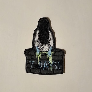 May include: Embroidered patch featuring a woman with long black hair sitting on a brick wall with the text "7 DAYS!" in blue and green lettering.