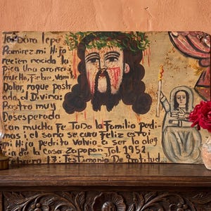 Op de afbeelding: Een rechthoekig volkskunstschilderij op een lichte achtergrond met een centraal portret van een figuur met een doornenkroon en bloed, vergezeld door een kleinere figuur met een kaars en uitgebreide handgeschreven Spaanse tekst uit 1952.