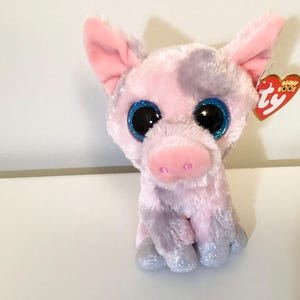May include: A pink plush pig with large blue glittery eyes and a pink snout. The pig has pink ears and glittery silver hooves. A red and white Ty tag is attached to the ear.