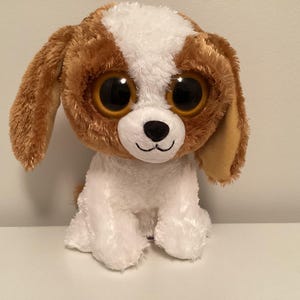 May include: A brown and white plush dog toy with large, black eyes. The dog has a white muzzle and brown ears.