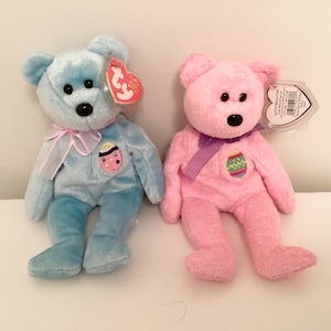 May include: Two plush beanie baby toys, one blue and one pink, with embroidered Easter egg designs and Ty tags.