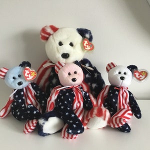 Pode incluir: Quatro ursos de pelúcia Beanie Baby vestindo roupas patrióticas vermelho, branco e azul. Os ursos estão todos sentados em uma superfície branca.