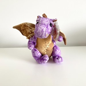 May include: Purple and brown plush dragon with wings. The dragon has a small tag attached to its wing.