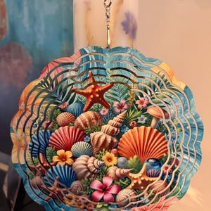 May include: A circular metal wind spinner featuring a vibrant tropical scene with various seashells, orange and red starfish, and colorful flowers. The design includes intricate cutouts and a silver metal hook at the top for hanging display.