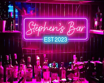 May include: A neon sign with pink and blue lights that reads "Stephen's Bar EST 2023". The sign is hanging above a bar counter with bottles of liquor lined up on the counter.