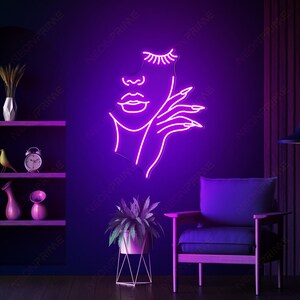 May include: A neon sign depicting a woman's face with closed eyes and a hand touching her cheek. The sign is pink and is mounted on a wall.