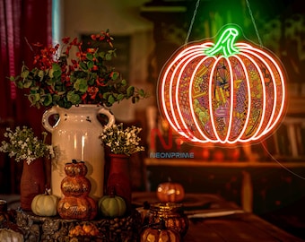Op de afbeelding: Een neon-bord in de vorm van een pompoen met een gedetailleerd oranje en geel ontwerp. Het bord hangt aan een ketting en wordt verlicht met een warme oranje gloed. Op een houten tafel op de achtergrond staan ​​verschillende kleine pompoenen en andere herfstdecoraties.