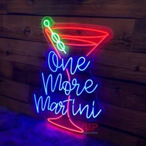 Pu&ograve; includere: Insegna al neon a forma di bicchiere da Martini con le parole "One More Martini" in neon blu. Il contorno del bicchiere da Martini &egrave; rosso, con un'oliva verde e uno stelo. Su sfondo di legno.