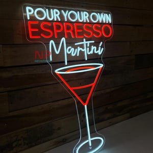 Pu&ograve; includere: Un'insegna al neon a forma di bicchiere da Martini con le parole "POUR YOUR OWN ESPRESSO MARTINI" in bianco e rosso. L'insegna &egrave; montata su una parete di legno.