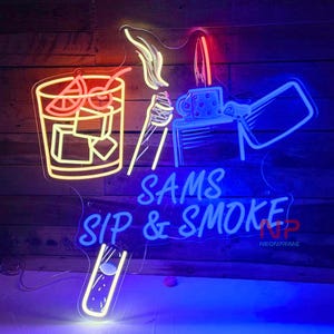 Pu&ograve; includere: Insegna al neon con un cocktail, cubetti di ghiaccio e un design di accendino. L'insegna dice "SAMS SIP & SMOKE" in neon blu. Il cocktail &egrave; delineato in neon giallo, con accenti rossi. Lo sfondo &egrave; un muro di legno.