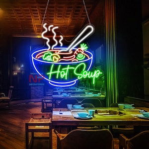 May include: Neon sign featuring a blue bowl of hot soup and the text "Hot Soup" in green. The sign is suspended from the ceiling above a table with chairs.