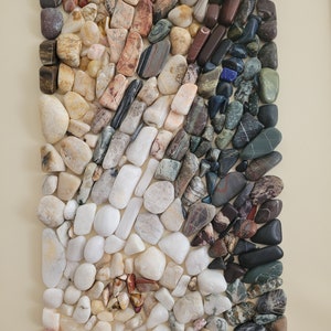 以下が含まれることがあります： 様々な色と模様の滑らかで磨かれた石のコレクションが、長方形に配置されています。石は主に白、グレー、茶色で、赤、緑、青のアクセントがいくつかあります。