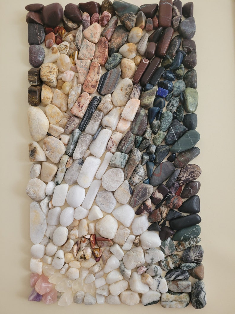 以下が含まれることがあります： 様々な色と模様の滑らかで磨かれた石のコレクションが、長方形に配置されています。石は主に白、グレー、茶色で、赤、緑、青のアクセントがいくつかあります。