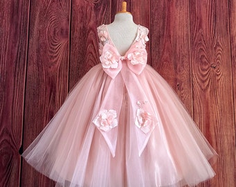 May include: A pink tulle dress with a large bow and floral embellishments. The dress has a low back and is perfect for a special occasion.