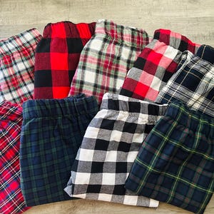 Peut inclure: Un assortiment de pantalons de pyjama à carreaux de différentes couleurs, dont le rouge, le noir, le blanc et le vert. Les pantalons sont pliés et disposés en cercle, mettant en valeur les différents motifs et couleurs.
