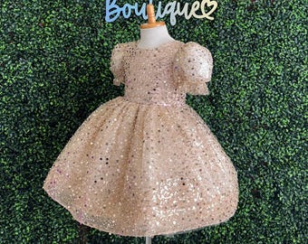 May include: A gold sequined dress with puff sleeves. The dress is on a mannequin and has a tulle skirt.