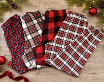 Op de afbeelding: Vier loungebroeken met diverse ruitpatronen en buffalo-ruiten in rood, zwart, wit en blauw. Elke broek heeft een elastische tailleband en een recht model, wat een collectie feestelijke nachtkleding voor de feestdagen laat zien.