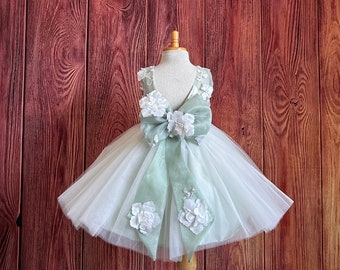 May include: A sage green tulle dress with a large bow and white floral embellishments.