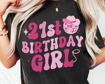 May include: Black t-shirt with pink text that says "21st Birthday Girl" with a pink disco ball and cowboy hat graphic.
