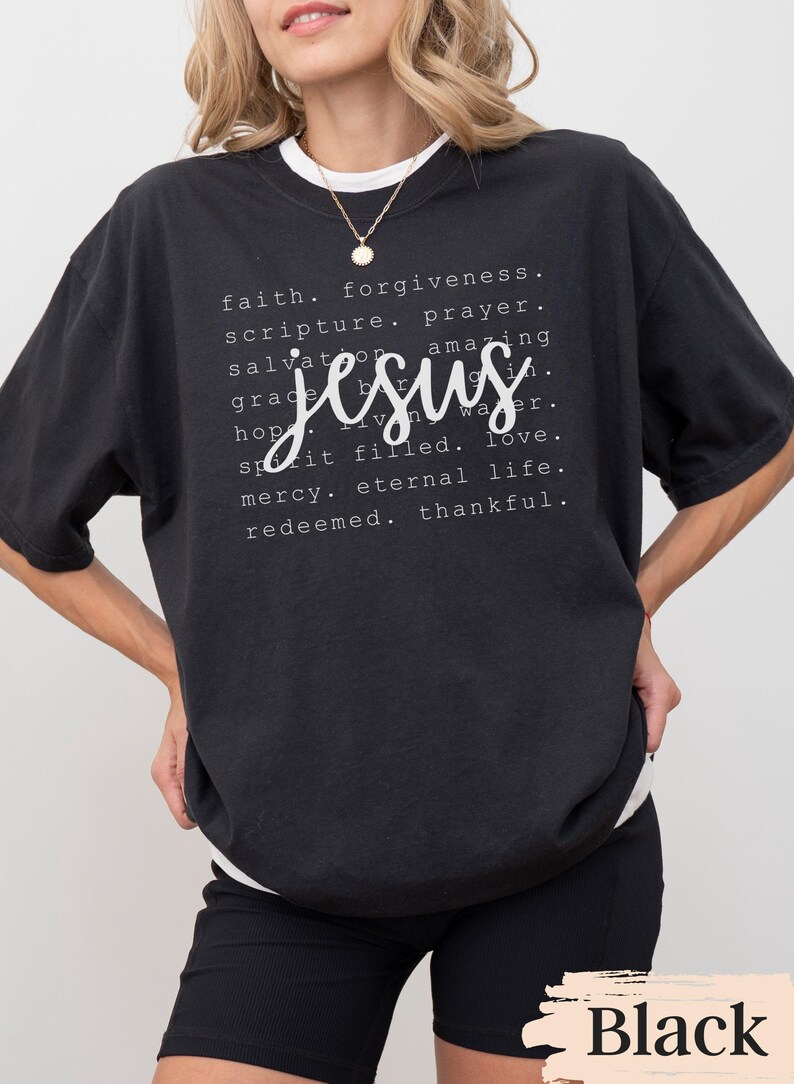 May include: Black t-shirt with the word "Jesus" in a cursive font, surrounded by words like "faith," "forgiveness," and "love." The shirt has a white crew neck and is worn with black shorts.