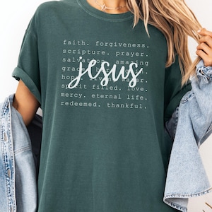 May include: Blue Spruce colored t-shirt with the word "Jesus" in a cursive font. The shirt features a list of words including "faith", "forgiveness", and "love". The shirt is a comfortable, casual style.