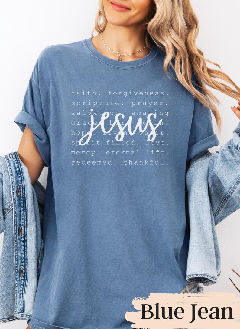 May include: A blue t-shirt with the word "Jesus" in a cursive font, surrounded by words like "faith," "forgiveness," and "eternal life." The shirt has rolled-up sleeves and the text "Blue Jean" at the bottom.