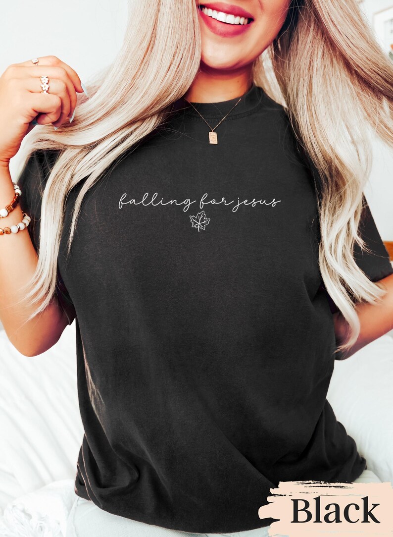 May include: Black t-shirt with the phrase "falling for jesus" in cursive script and a small maple leaf graphic. The word "Black" is printed at the bottom of the shirt. A casual, comfortable style.