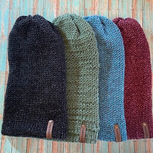 May include: Four knitted beanies in black, green, blue, and burgundy with a leather tag that says "Designed by Me" on each.