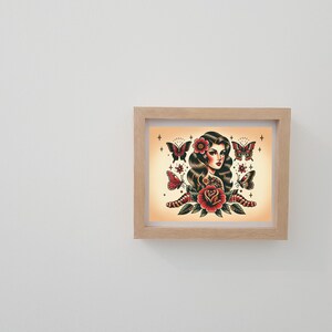 May include: A framed print of a woman with long dark hair and a red rose. She is surrounded by butterflies and stars. The print is in a light wood frame.