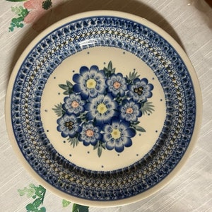 May include: A white ceramic plate with a blue and white floral design. The plate has a decorative border of blue and gold swirls.