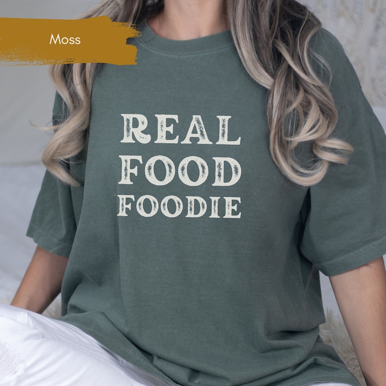 May include: A moss green t-shirt with the text "REAL FOOD FOODIE" printed in white.
