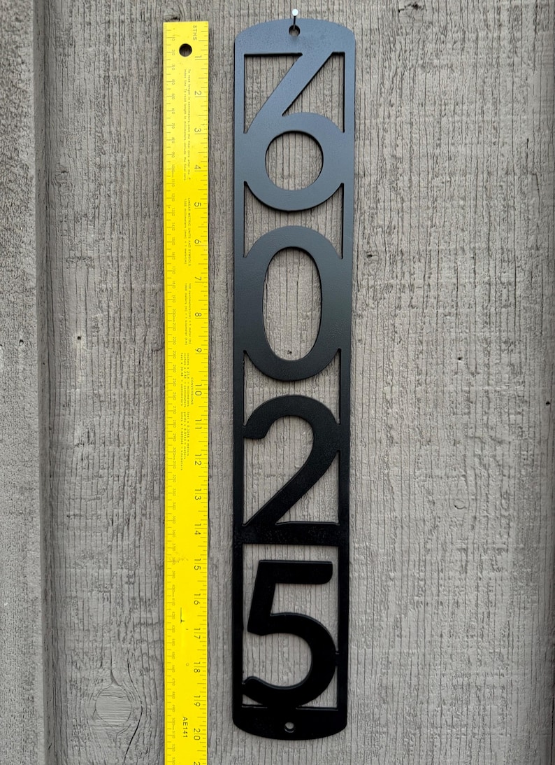 May include: Black metal house number plaque with the numbers 2025 cut out. The plaque is 20 inches tall and is shown next to a ruler.