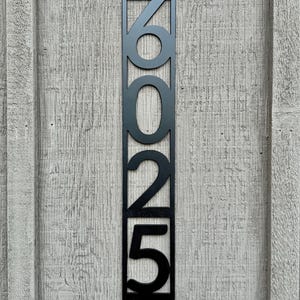 May include: Black metal house number plaque with the numbers 6025 displayed vertically.