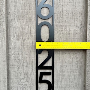 May include: Black metal house number plaque with the numbers 2025. The plaque is approximately 10 inches tall and is mounted on a wooden surface.