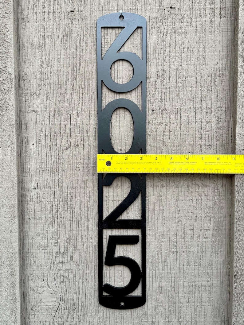May include: Black metal house number plaque with the numbers 2025. The plaque is approximately 10 inches tall and is mounted on a wooden surface.