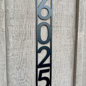 May include: Black metal house number plaque with the numbers 2025 displayed vertically.