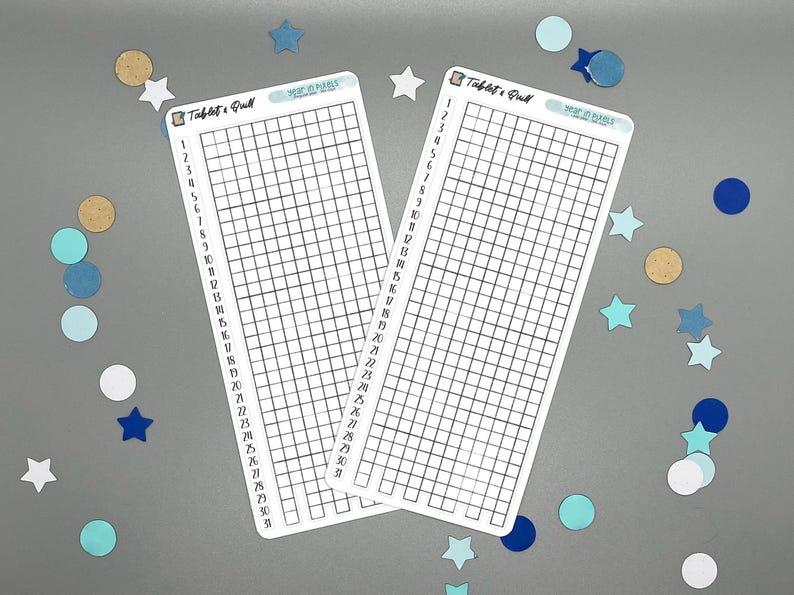 May include: Two white rectangular stickers with a grid pattern and the text "Tablets & Quill" and "Year of Goals". The stickers are surrounded by blue, white, and gold confetti in star and circle shapes.