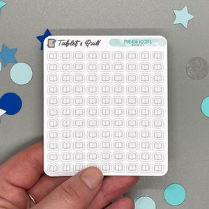May include: A sheet of white stickers with small, outlined book icons. The sticker sheet has the text "Tablet & Quill" and "media icons BOOKS". The background is gray with blue and white star and circle decorations.