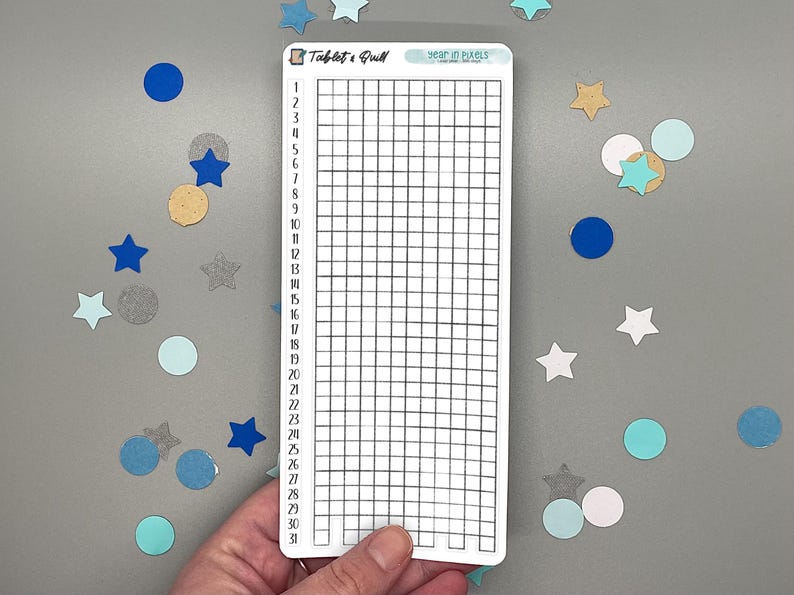 May include: A white rectangular sticker with a grid for tracking daily habits. The sticker has the text "Tablet & Quill" and "year in pixels". The background has blue, silver, and gold confetti in star and circle shapes.