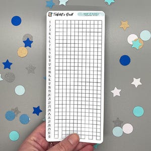 May include: A white rectangular sticker with a grid for tracking daily habits. The sticker has the text "Tablet & Quill" and "Year in Pixels". Scattered around are blue, silver, and gold star and circle confetti.