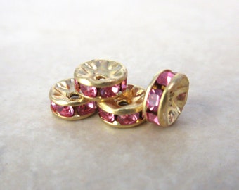 May include: Four gold-toned metal bead caps with pink rhinestones. The bead caps are round and have a raised edge.