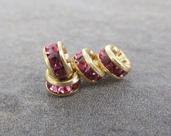 May include: Four gold-toned bead spacers with pink rhinestones. The spacers are round and have a smooth surface.