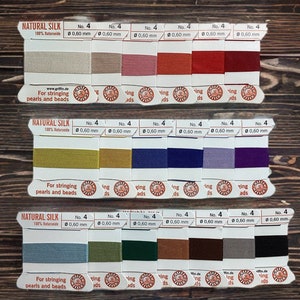 May include: Three spools of natural silk thread in various colors, including beige, pink, red, and burgundy. Each spool is labeled "NATURAL SILK" and "No. 4, 0.60 mm." The packaging states the thread is for stringing pearls and beads.