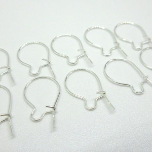 May include: Ten silver earring hooks, also known as ear wires, are arranged on a white surface. The hooks are made of metal and have a simple, classic design.