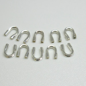 May include: Ten silver-toned metal crimp beads, each shaped like a U, are arranged in two rows on a white surface.
