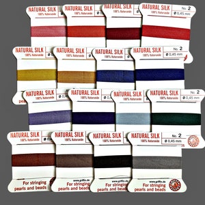 May include: A collection of spools of Natural Silk thread in various colors, including red, brown, and blue. Each spool is labeled with "NATURAL SILK" and "100% Naturseide". The thread is 0.45 mm in diameter. Text at the bottom reads "For stringing pearls and beads".