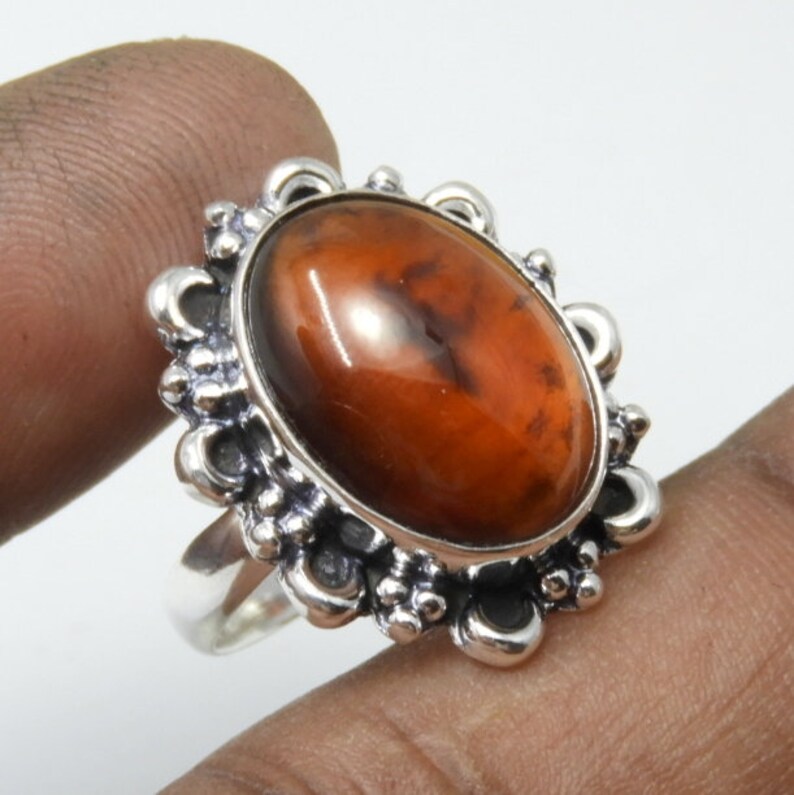 May include: A silver ring with an oval-shaped amber gemstone set in a decorative floral design.