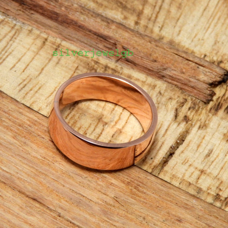 May include: A simple, polished, rose gold band ring.